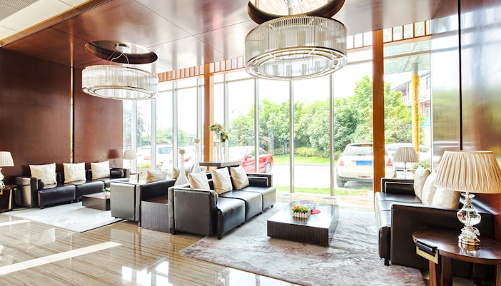 Modern hotel reception with leather sofas, large windows, and elegant chandeliers.