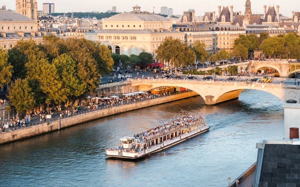 Seine River cruise boat passing under a bridge in Paris, France, with cityscape in the background.