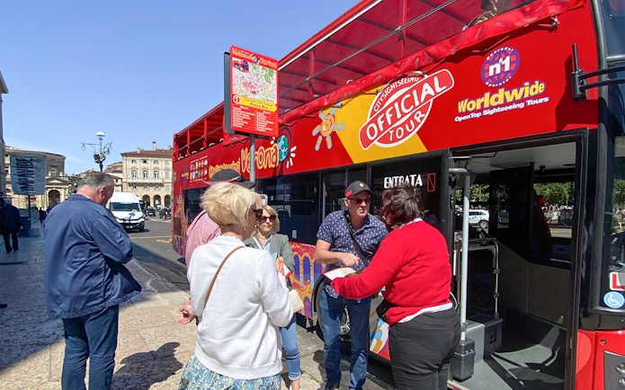 Tourists boarding a red hop-on hop-off bus in Verona for a sightseeing tour.