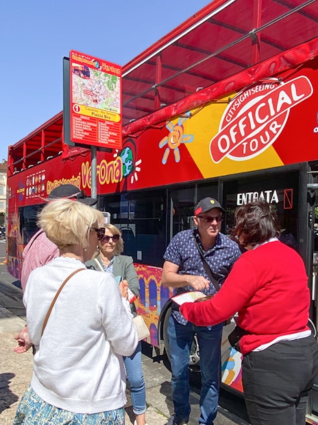 Tourists boarding a red hop-on hop-off bus in Verona for a sightseeing tour.