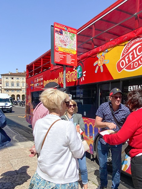 Tourists boarding a red hop-on hop-off bus in Verona for a sightseeing tour.