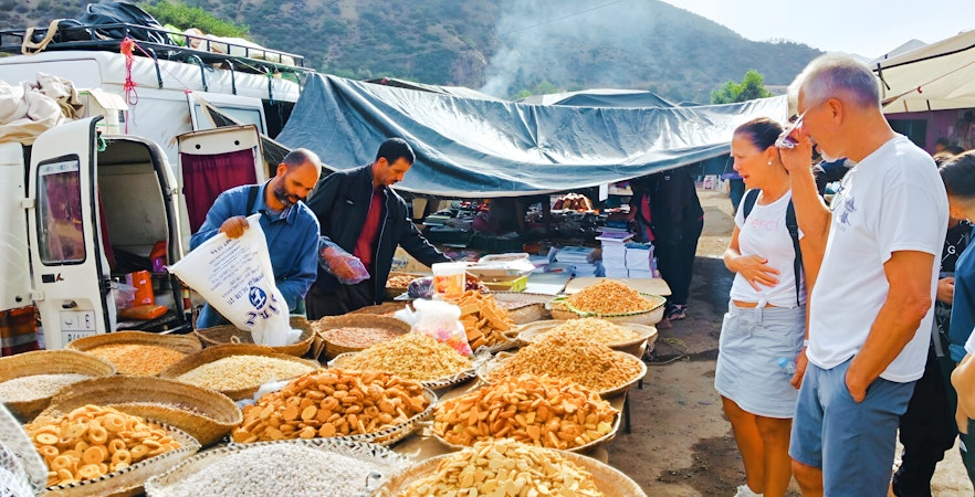 Market stall with local snacks and tourists in Ourika Valley, Morocco.