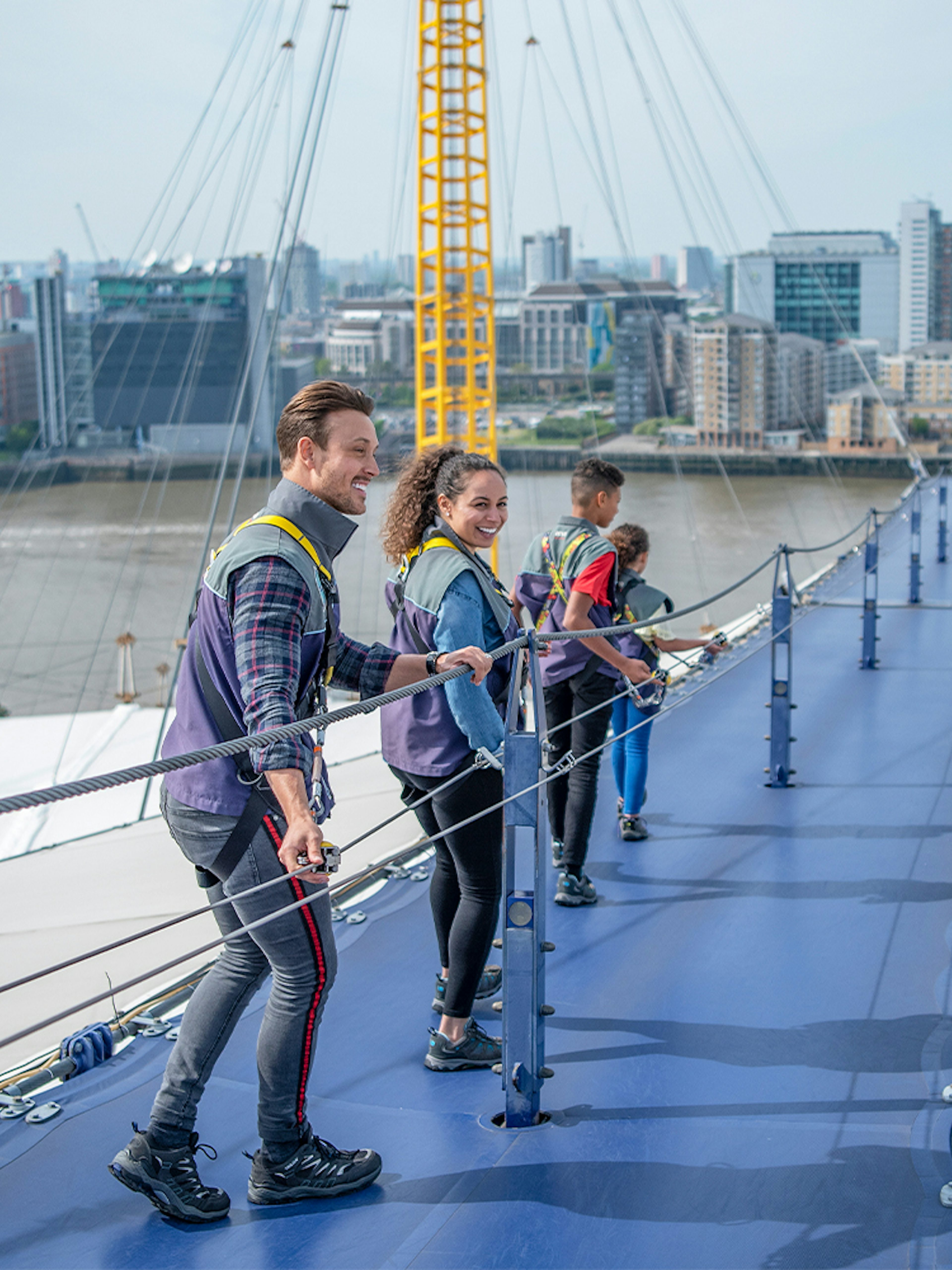Visitors climbing the O2 roof walkway with London skyline in the background.