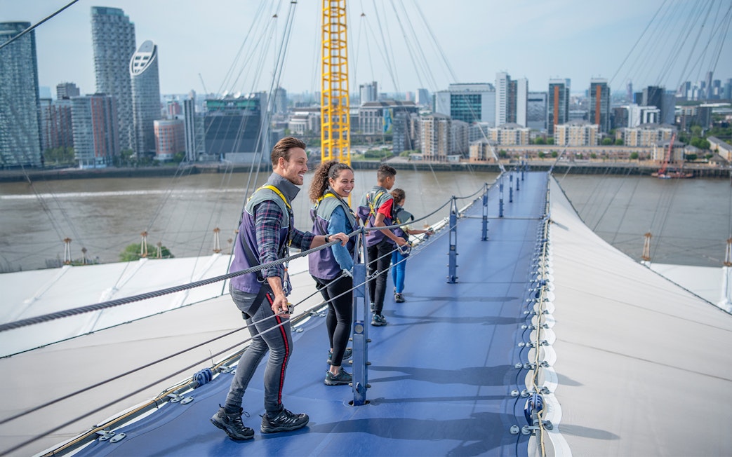 Visitors climbing the O2 roof walkway with London skyline in the background.