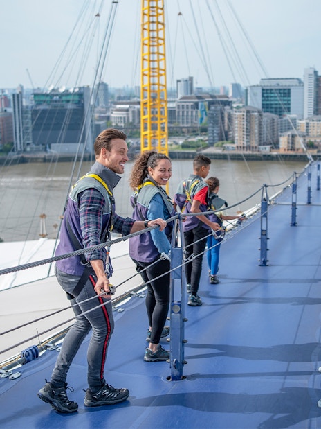 Visitors climbing the O2 roof walkway with London skyline in the background.