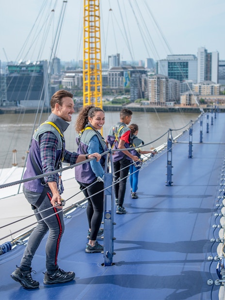 Visitors climbing the O2 roof walkway with London skyline in the background.