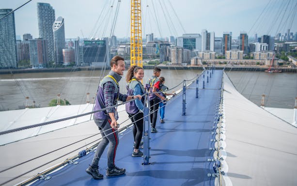 Visitors climbing the O2 roof walkway with London skyline in the background.
