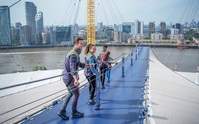 Visitors climbing the O2 roof walkway with London skyline in the background.