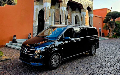 Black Mercedes van parked outside traditional Moroccan building, Marrakech transfer service.