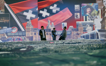 Three people exploring an interactive Amsterdam exhibit with city landmarks and flag.