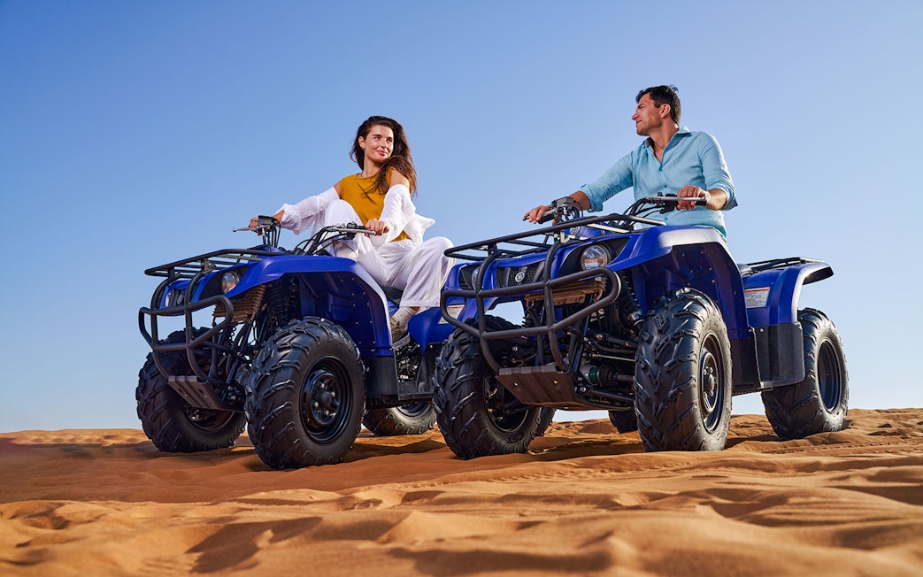 Two people riding quad bikes on sand dunes at Noble Camp Desert Safari.