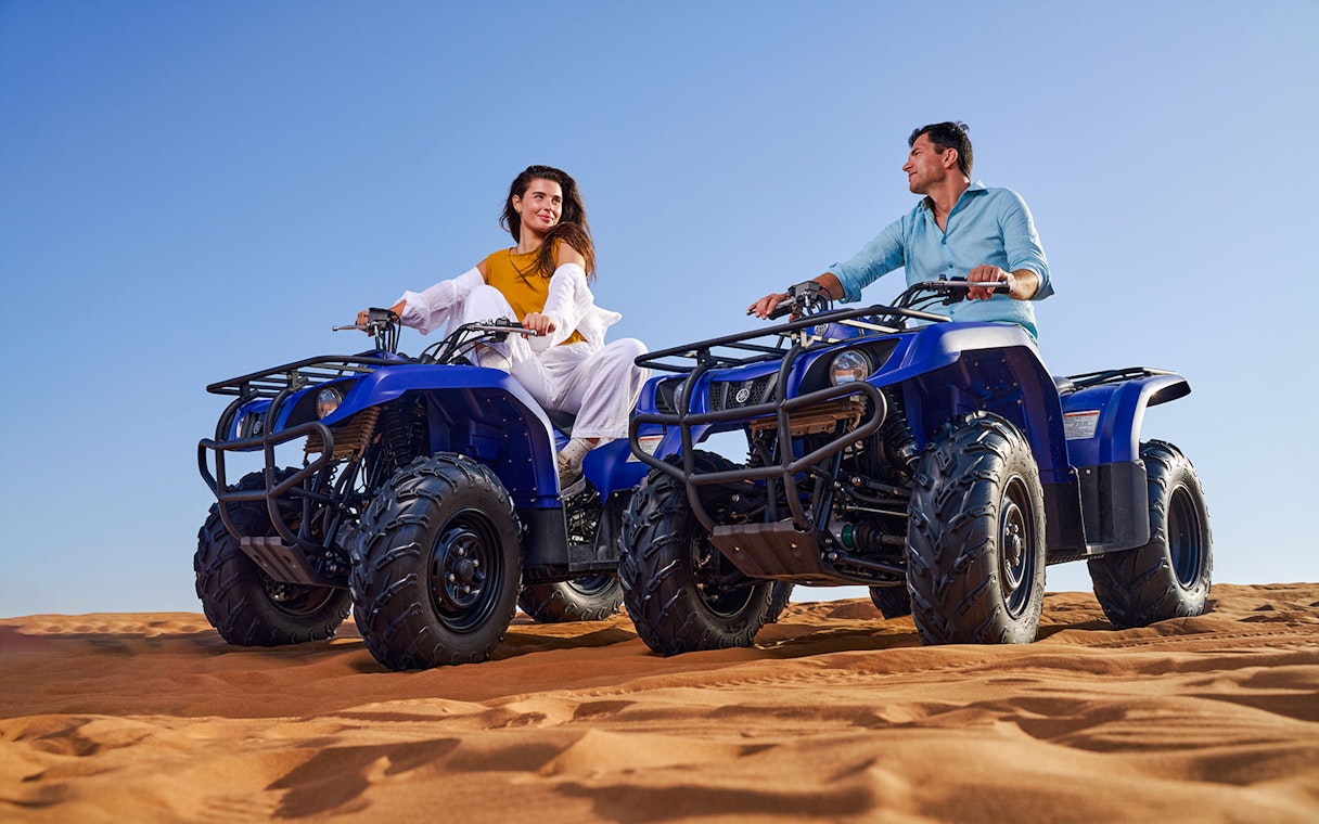 Two people riding quad bikes on sand dunes at Noble Camp Desert Safari.