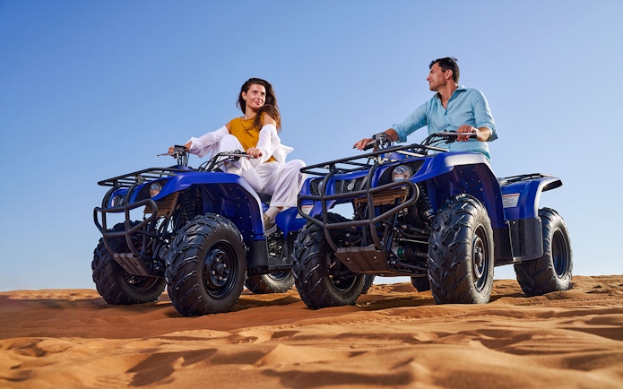 Two people riding quad bikes on sand dunes at Noble Camp Desert Safari.