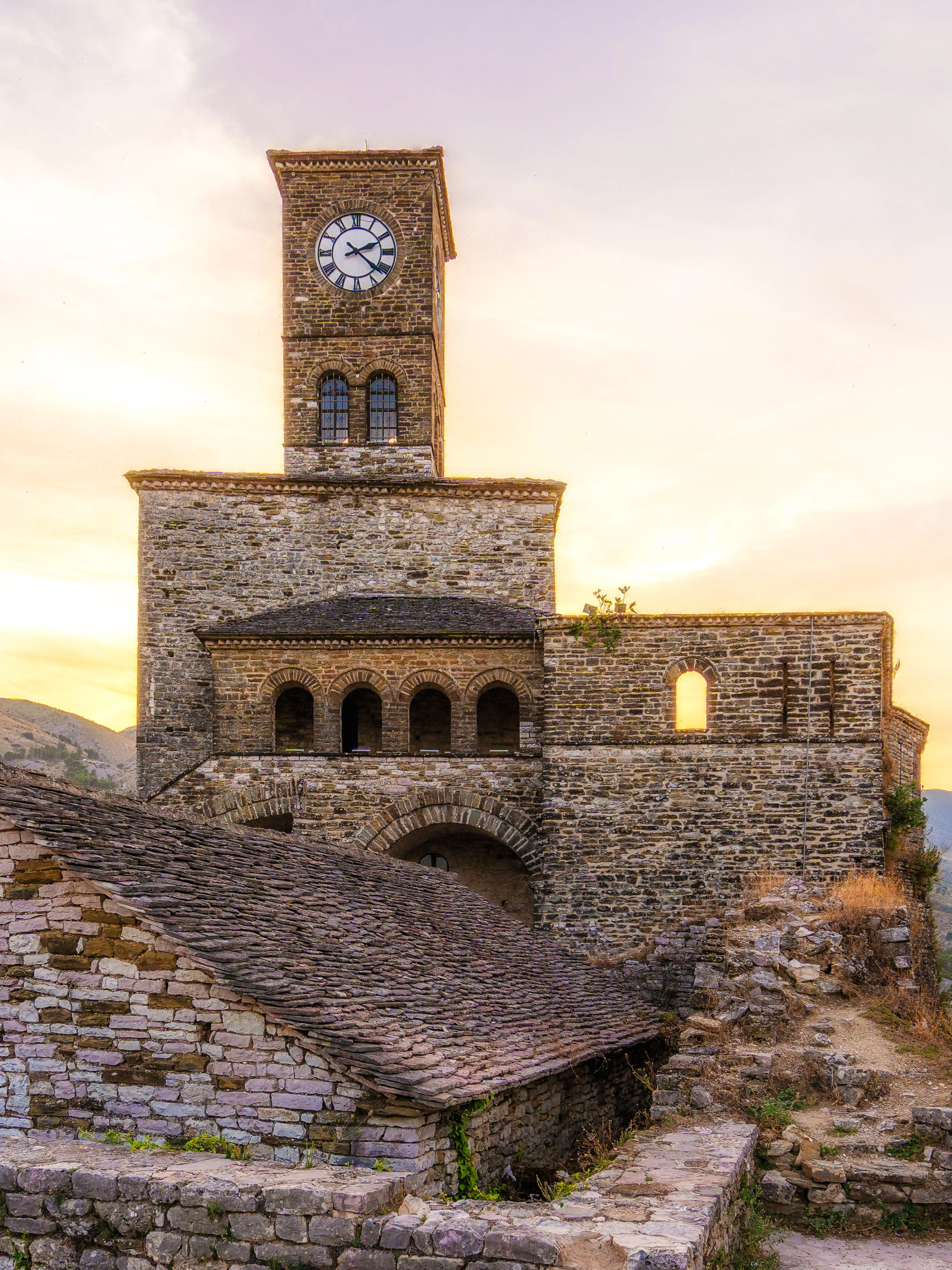 Gjirokastra Castle at sunset with clock tower and stone walls, Albania.