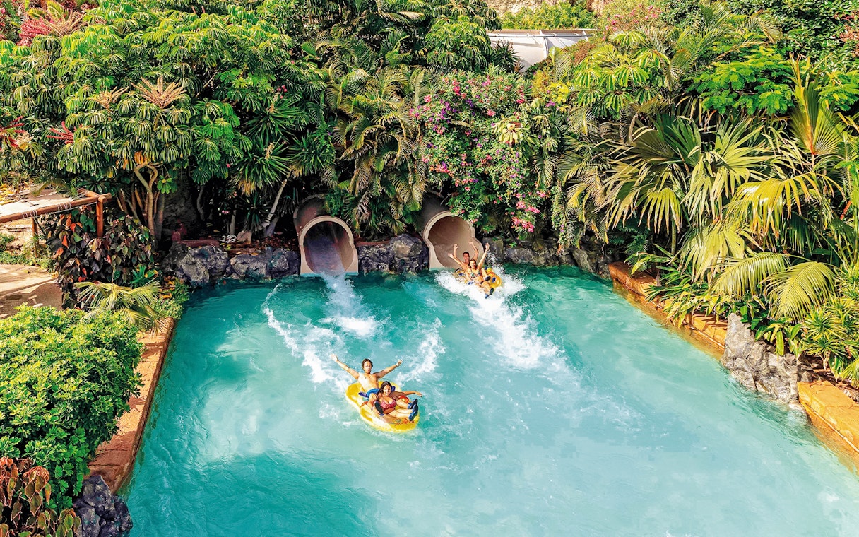 Tourists on water slide at Siam Park, Tenerife, surrounded by lush greenery.