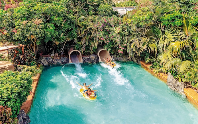 Tourists on water slide at Siam Park, Tenerife, surrounded by lush greenery.
