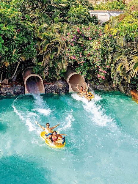 Tourists on water slide at Siam Park, Tenerife, surrounded by lush greenery.