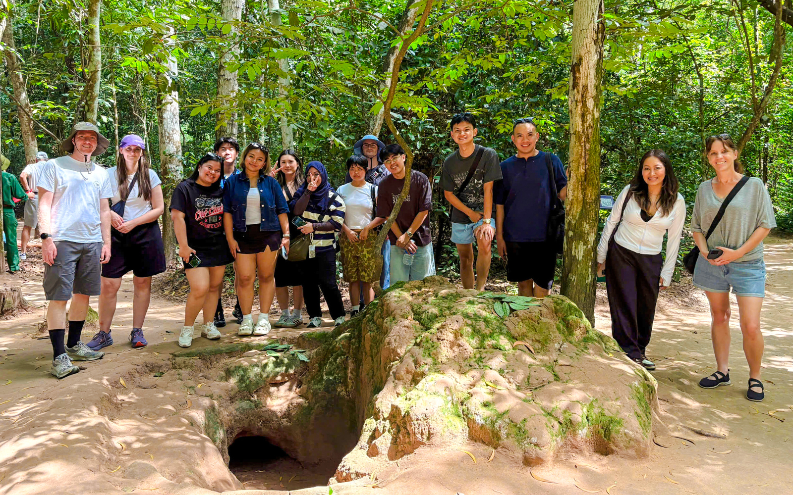 Tourists exploring Cu Chi tunnels with a guide in a forest setting.
