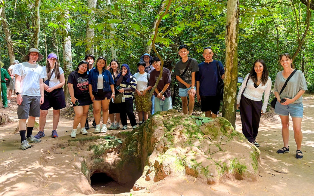Tourists exploring Cu Chi tunnels with a guide in a forest setting.