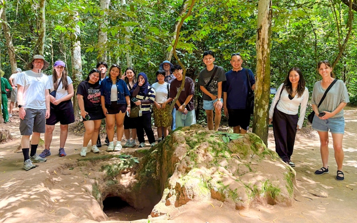 Tourists exploring Cu Chi tunnels with a guide in a forest setting.
