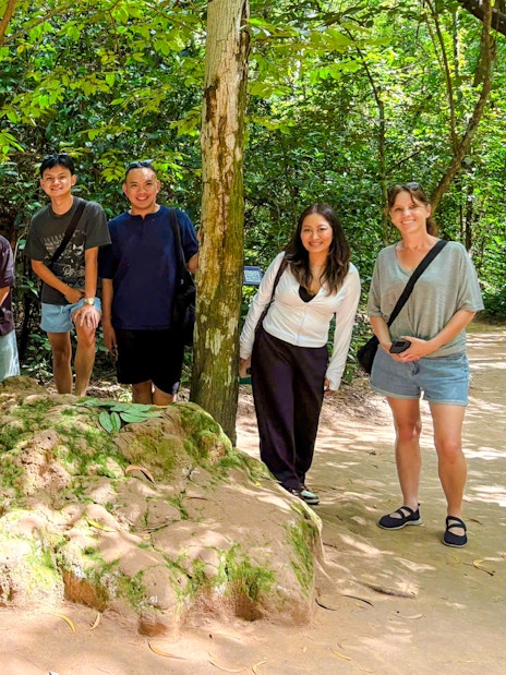 Tourists exploring Cu Chi tunnels with a guide in a forest setting.