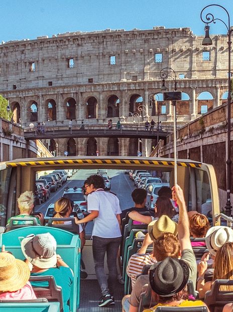 Tour guide interacting with tourists on a bus near the Colosseum in Rome.
