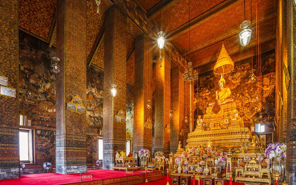 Golden Buddha statue inside Wat Pho temple, Bangkok, with ornate decorations and murals.