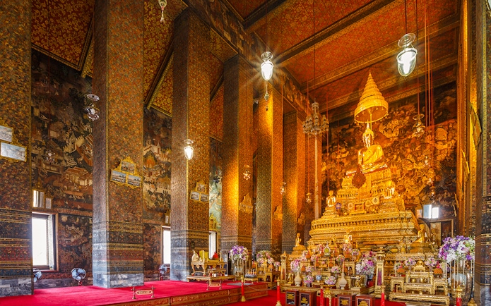 Golden Buddha statue inside Wat Pho temple, Bangkok, with ornate decorations and murals.