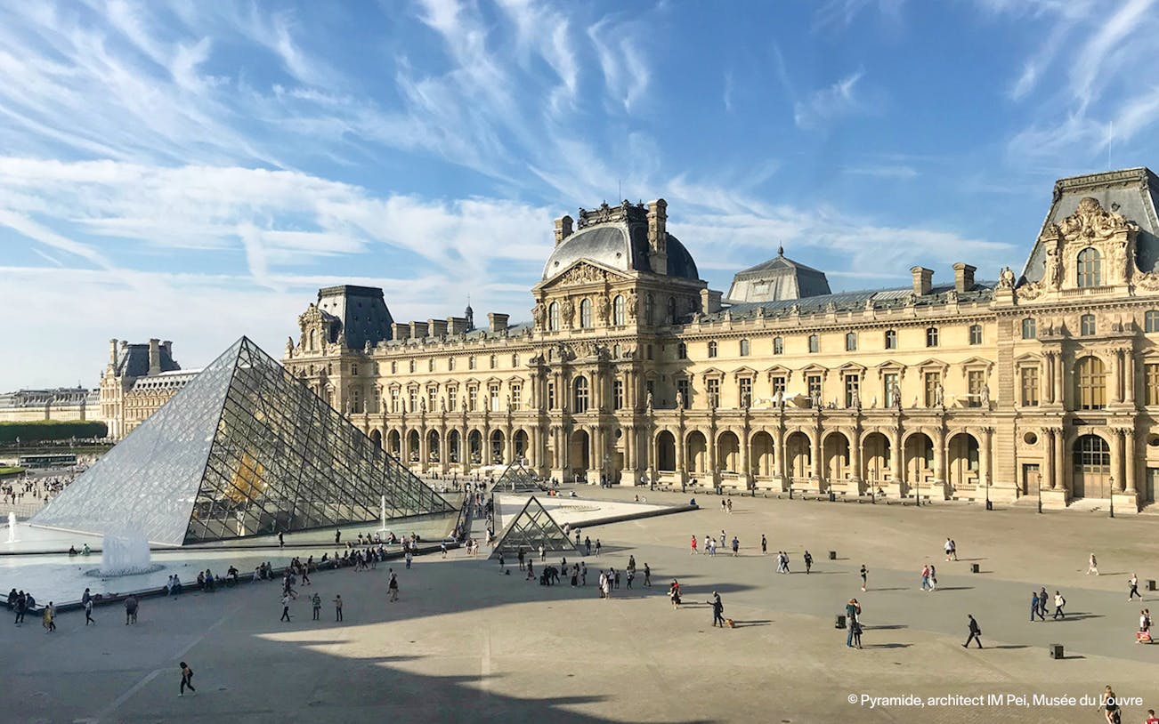 People walking near the Louvre glass pyramid in Paris, France.