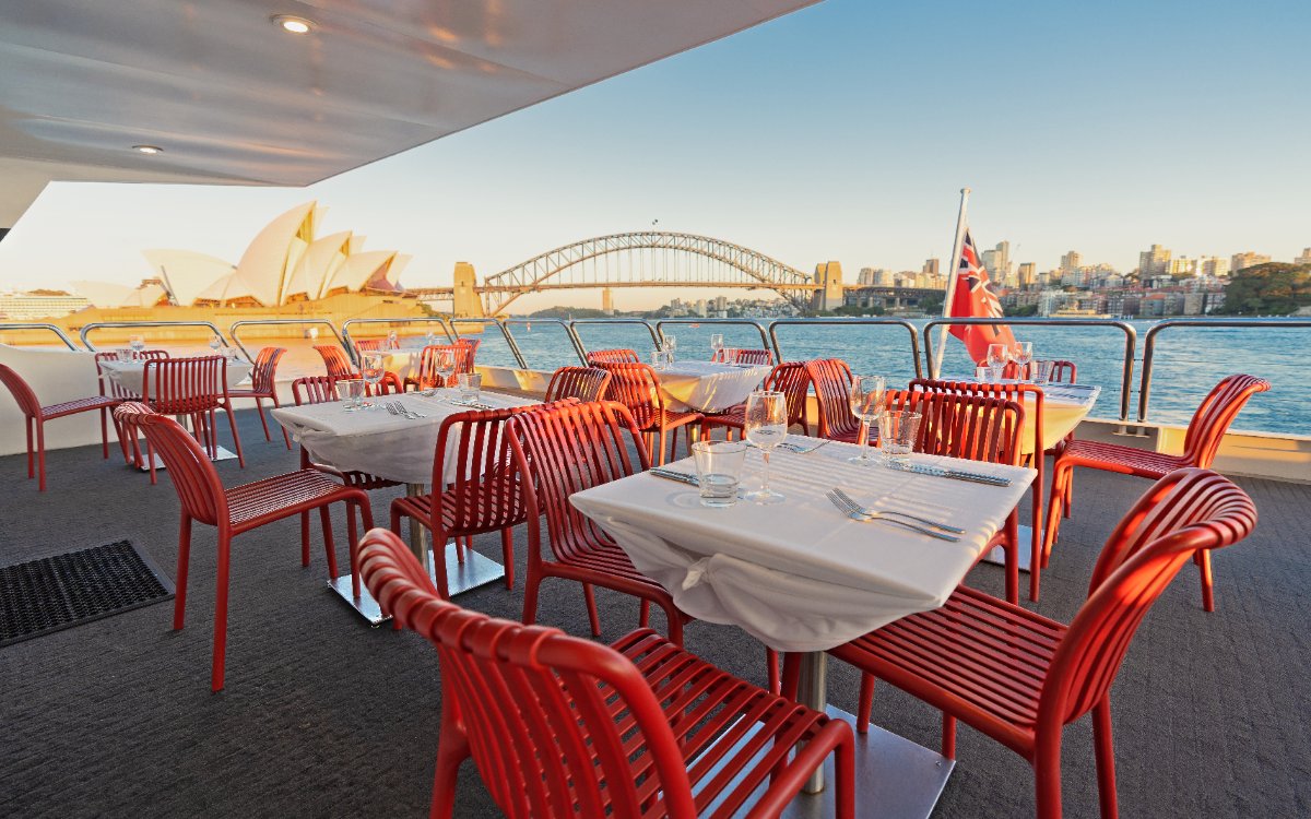 Luxury catamaran lunch cruise with table setup, Sydney Opera House and Harbour Bridge in view.
