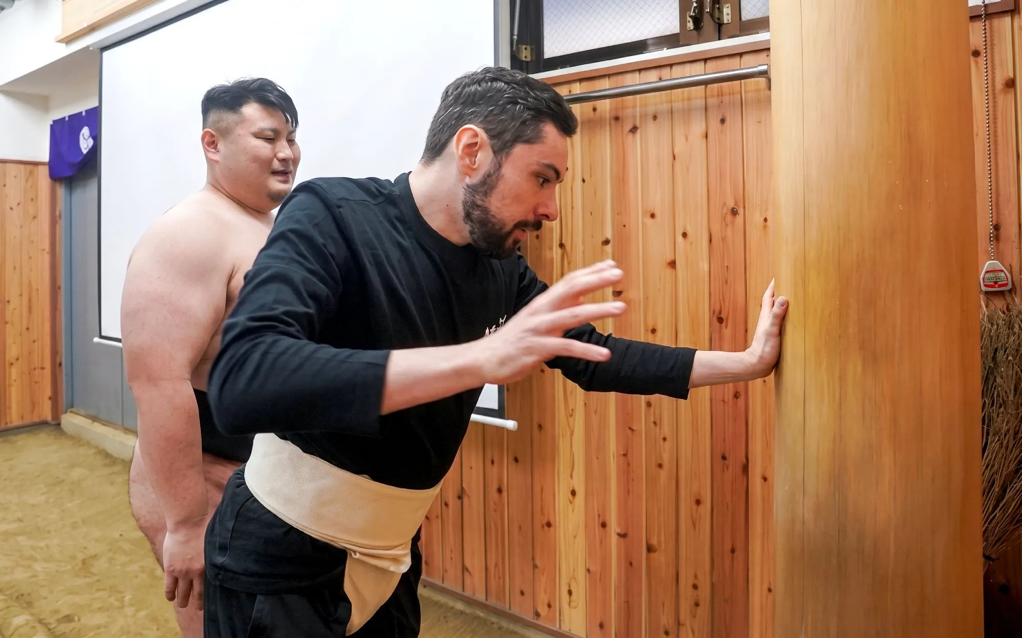 Sumo wrestler guides participant in training exercise at Tokyo dojo.