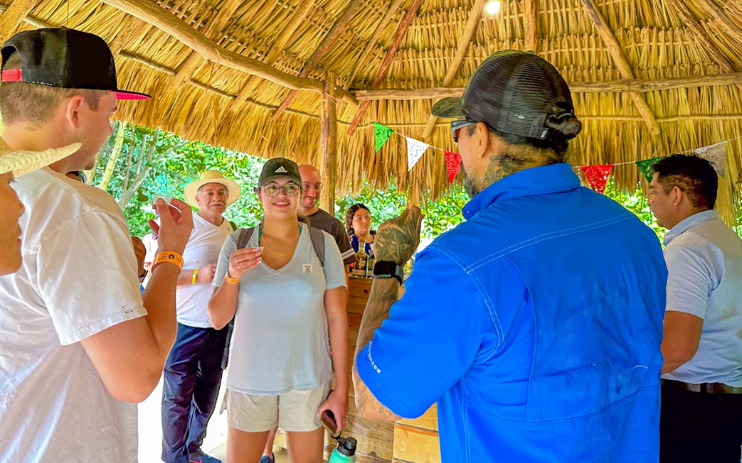 Tourists tasting tequila under a thatched roof during Chichen Itza tour.