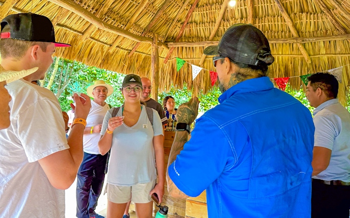 Tourists tasting tequila under a thatched roof during Chichen Itza tour.