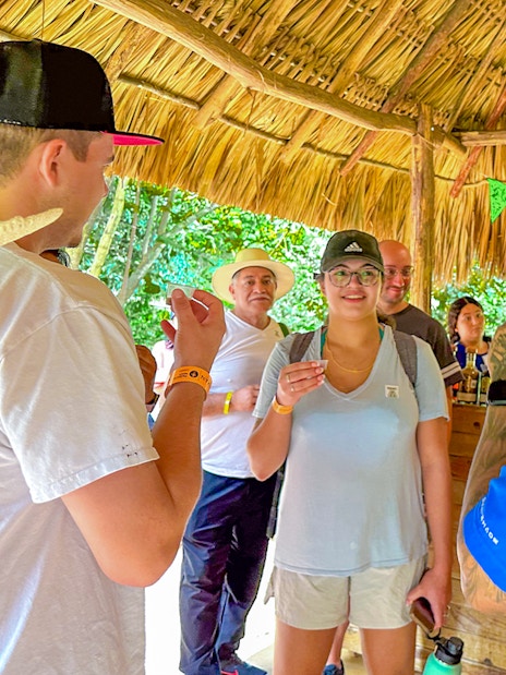Tourists tasting tequila under a thatched roof during Chichen Itza tour.