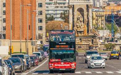 Barcelona hop-on hop-off bus near a historic monument on a city street.