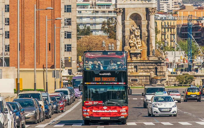 Barcelona hop-on hop-off bus near a historic monument on a city street.