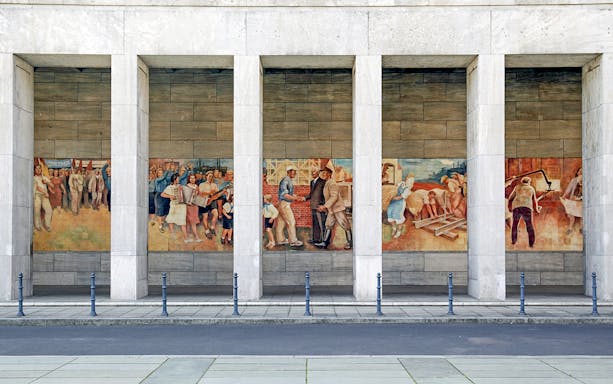 Berlin mural depicting historical scenes and workers at a memorial site.
