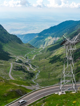 Transfagarasan mountain road winding through green valley with car and power lines.