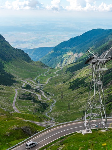Transfagarasan mountain road winding through green valley with car and power lines.