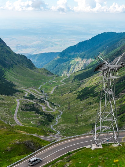 Transfagarasan mountain road winding through green valley with car and power lines.