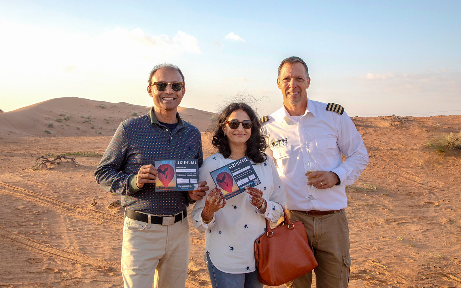 Couple with flight certificates and pilot in Ras Al Khaimah desert after hot air balloon ride.