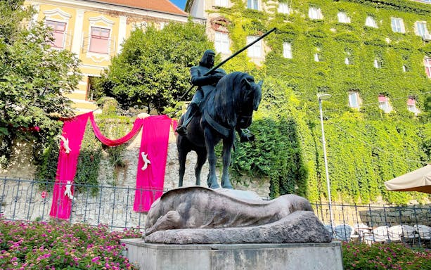 Statue of a knight on horseback in Zagreb, surrounded by greenery and pink decorations.