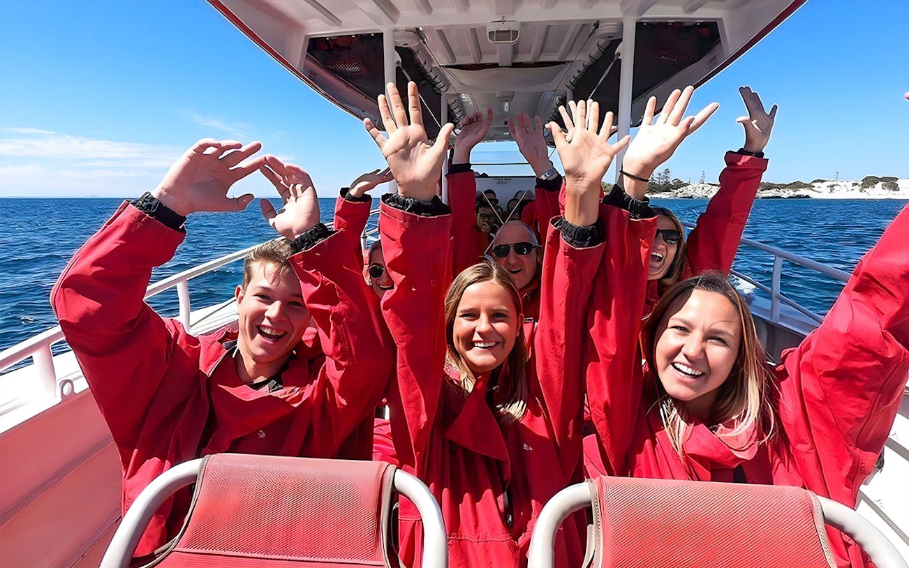 Tourists in red jackets enjoying a boat ride with Rottnest Island in the background.