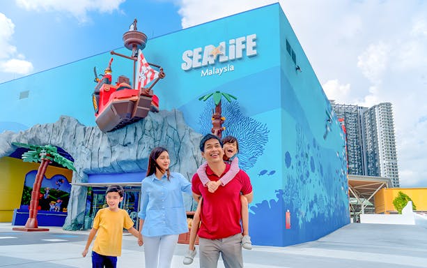 Family enjoying LEGOLAND® Malaysia Theme Park near SEA LIFE entrance with pirate ship display.