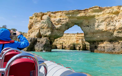 Tourist photographing rock formations from RIB boat near Benagil Caves, Algarve.