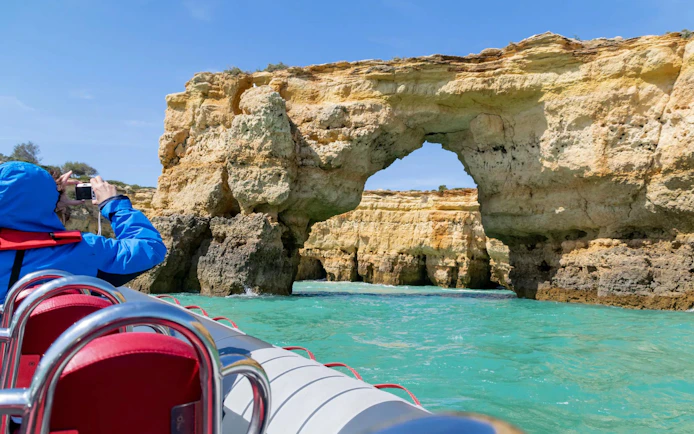 Tourist photographing rock formations from RIB boat near Benagil Caves, Algarve.