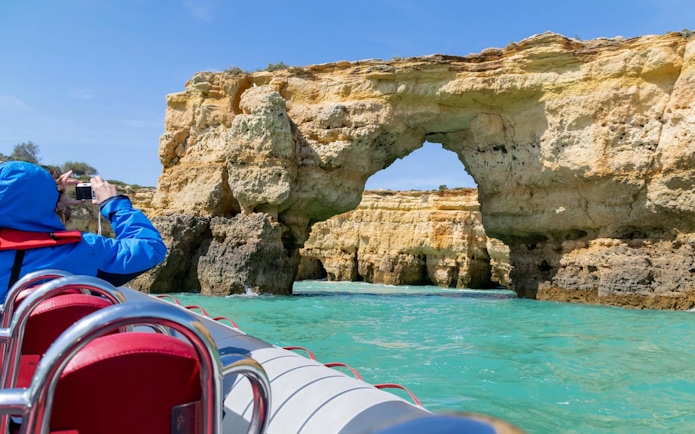 Tourist photographing rock formations from RIB boat near Benagil Caves, Algarve.
