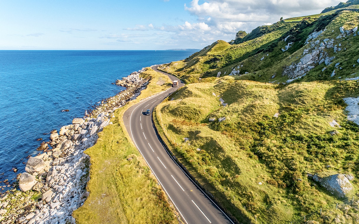 Coastal road along green hills and rocky shore on Game of Thrones tour in Belfast.