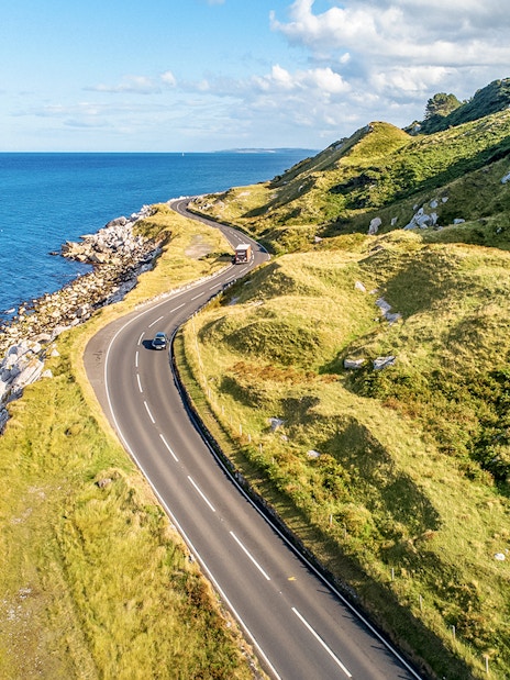 Coastal road along green hills and rocky shore on Game of Thrones tour in Belfast.