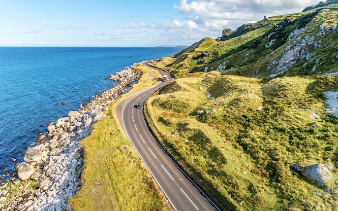 Coastal road along green hills and rocky shore on Game of Thrones tour in Belfast.